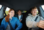 Personer sitter på i privatbil, smiler og er glade