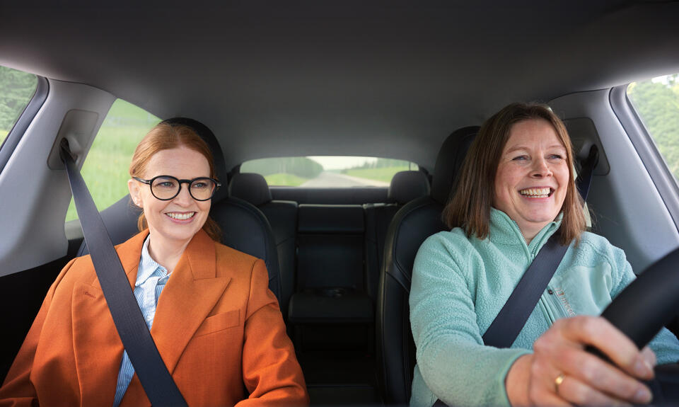Personer sitter på i privatbil, smiler og er glade