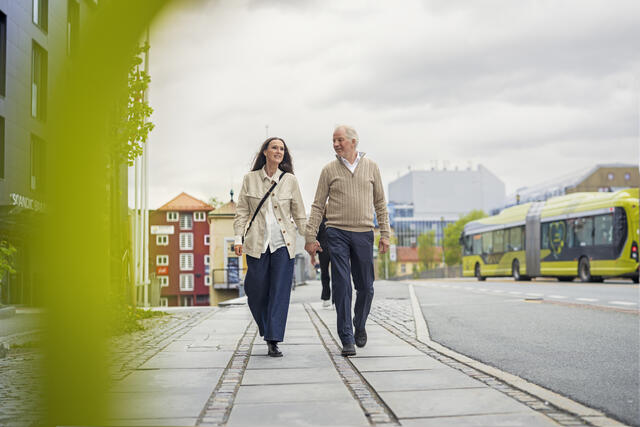 A woman and man walking towards us with a green bus in the background