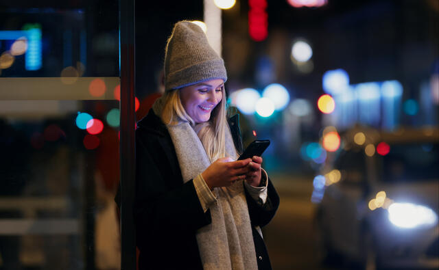 Dame om kvelden med lue med blikket mot mobilen