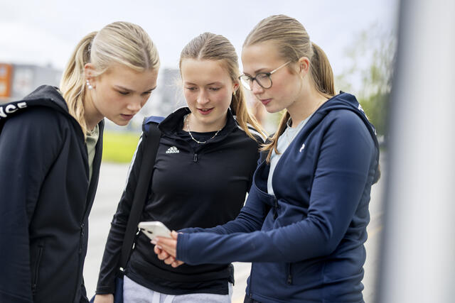 tre jenter som ser på mobilen