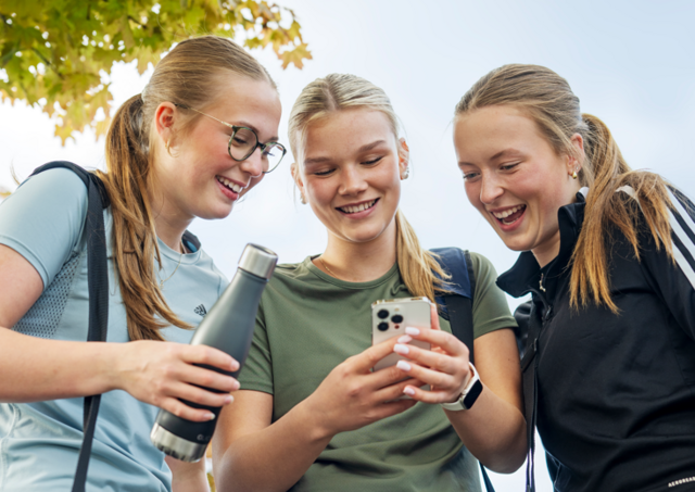 Tre jenter, ungdommer,  som ser på mobilen sammen