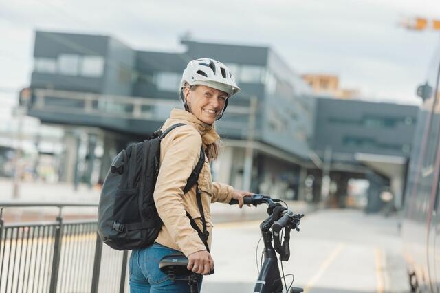 Kvinne med sykkel og sykkelhjelm smiler 