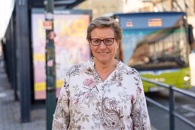 Grethe Fuglem Tennås, administrerende direktør i AtB. Smiler foran holdeplass med buss i bakgrunn